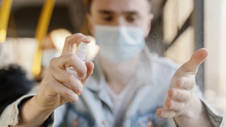Mann mit Maske desinfiziert sich die Hände im Bus