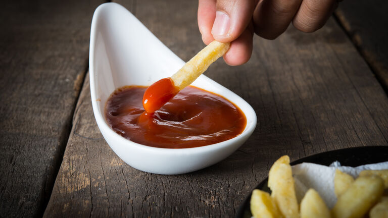 Person dippt eine Pommes in ein kleines Schälchen mit Ketchup