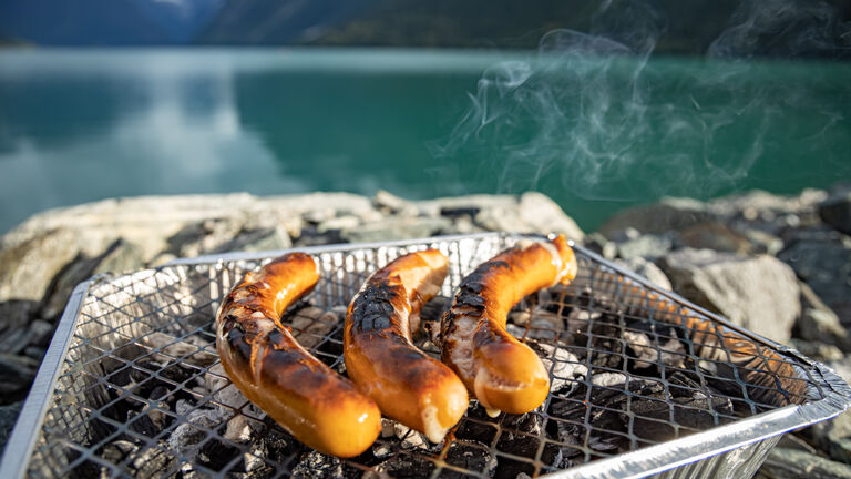 Drei Bratwürstchen liegen auf einem Einweggrill