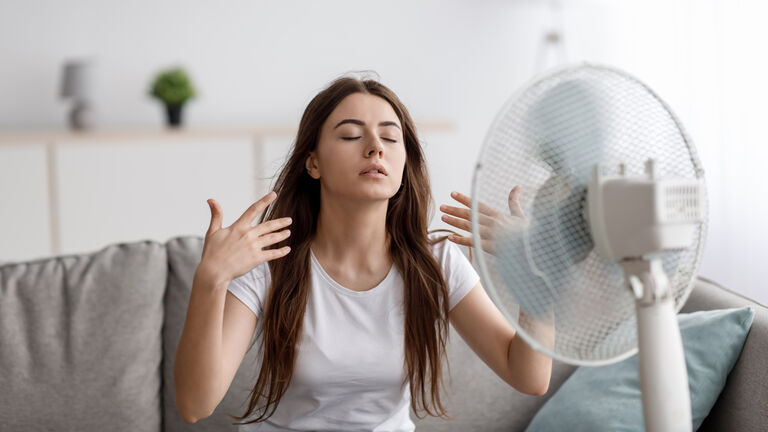 Frau sitzt vor einem Ventilator 