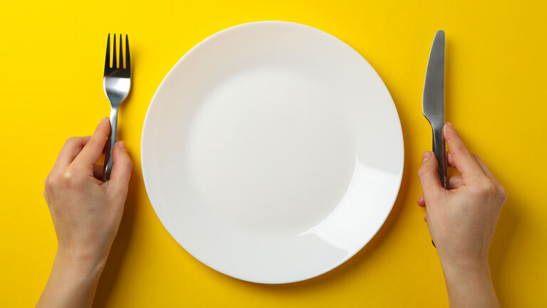Ein Teller und außen jeweils eine Hand mit Messer und Gabel vor gelbem Hintergrund
