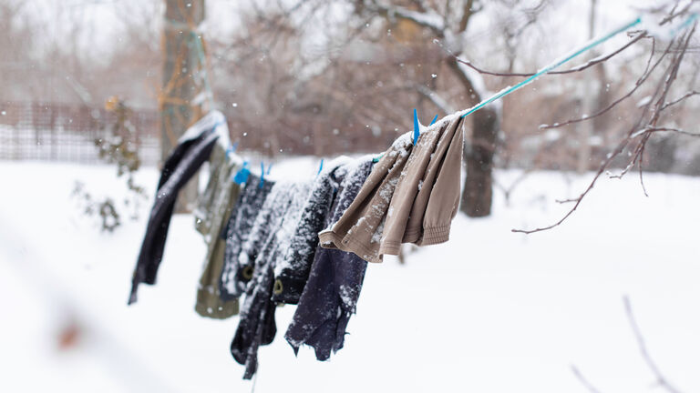 Wäsche hängt im Winter bei Schnee im Garten auf der Leine. Teilweise liegt Schnee auf der Wäsche.