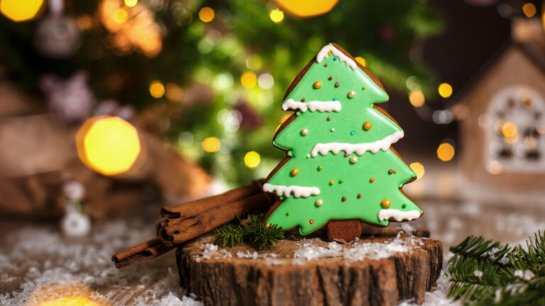 Ein Weihnachtsbaum aus Lebkuchen steht auf einer kleinen Baumscheibe. Im Hintergrund ist Lichterglanz zu sehen