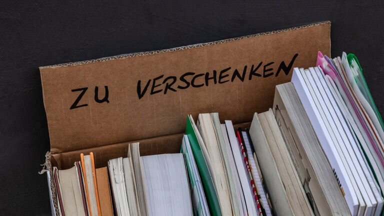 Pappkiste mit Büchern drin, von oben fotografiert. Auf der hinteren Kartonklappe steht "zu verschenken" drauf.