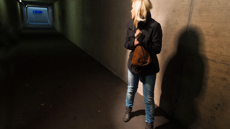 Blonde Frau mit Handtasche nacht im Tunnel dreht sich um, um zu schauen ob jeman dhinter ihr ist. Sie hat Angst.