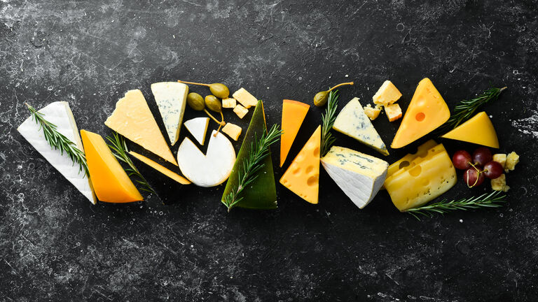 Verschiedene Käsesorten schön angerichtet auf eienr schwarzen Schieferplatte, von oben fotografiert.