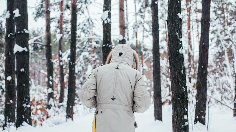 Mann mit hellem Mantel geht im schneebedeckten Wald spazieren