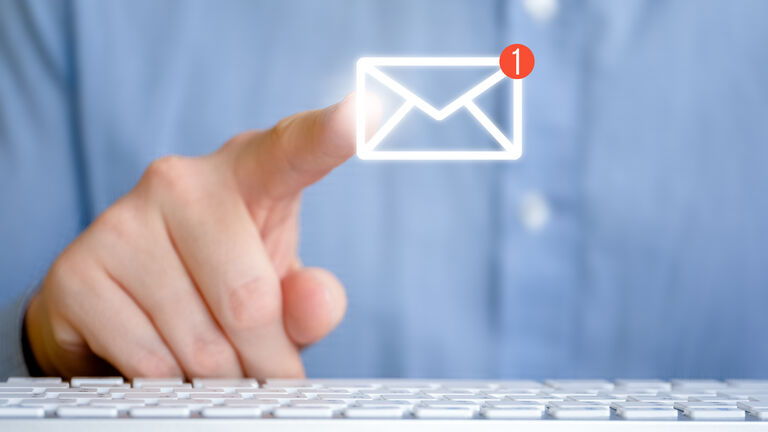 Eine Person sitzt vor einem Bildschirm und einer Tastatur und zeigt mit dem Finger auf ein abstraktes E-Mail-Symbol.