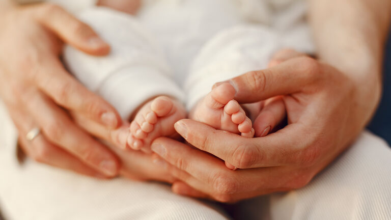 Beine und Füße eines Babys werden von der Mutter gehalten 
