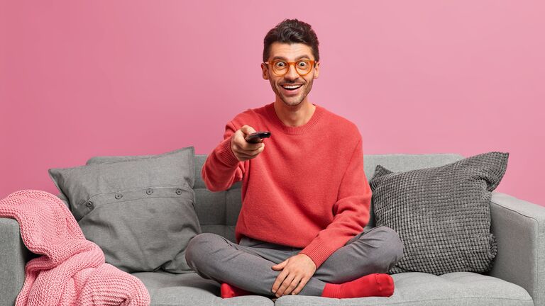 Ein Mann sitzt auf einem Sofa und bedient eine TV-Fernbedienung