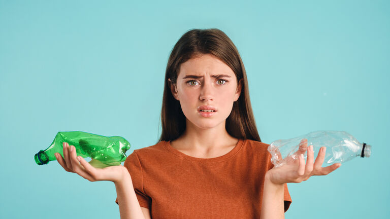 Ein junge Frau hält mit verärgertem Blick zwei leere zerknautschte Plastikflaschen in die Kamera
