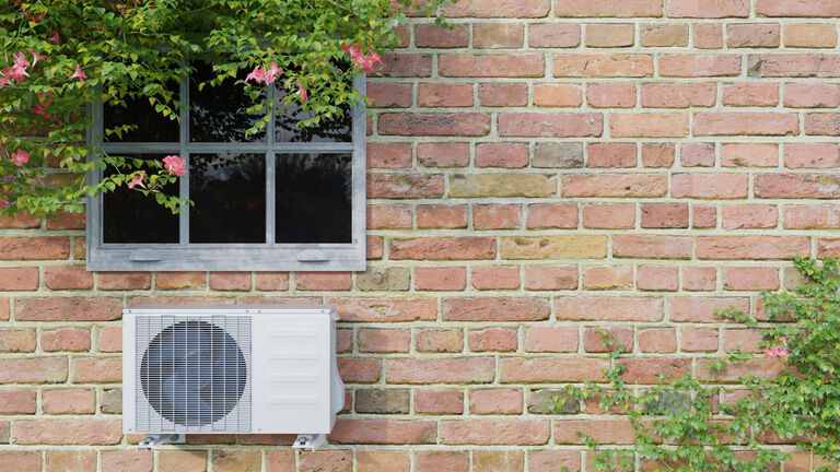 An einer Außenwand eines Backsteingebäudes unterhalb eines Fensters hängt ein Klima-Split-Gerät
