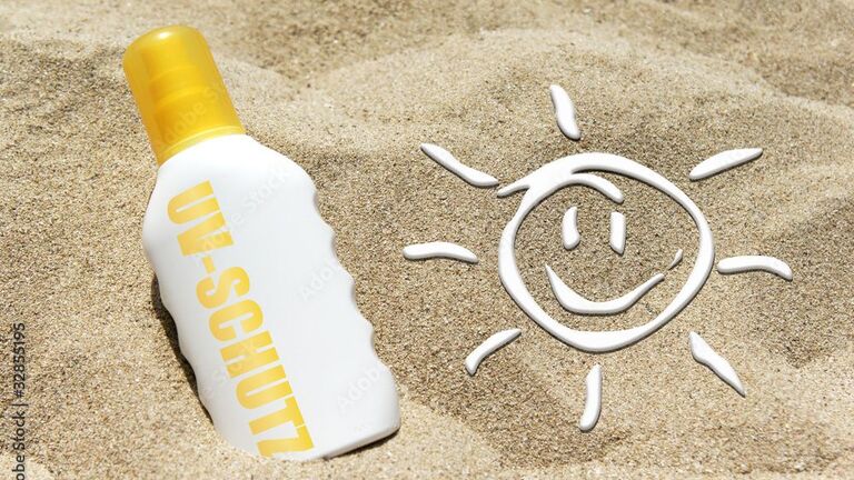 lachendes Smiley aus Sonnencreme und Sonnencremeflasche im Sand