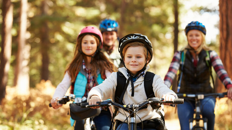 Eine vierköpfige Familie fährt mit dem Fahrrad durch den Wald. Alle tragen einen Fahrradhelm.