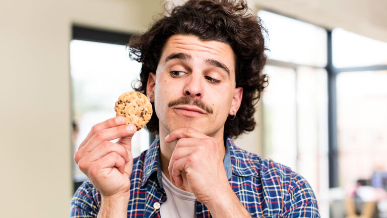 Ein junger Mann schaut skeptisch auf einen Keks in seiner Hand