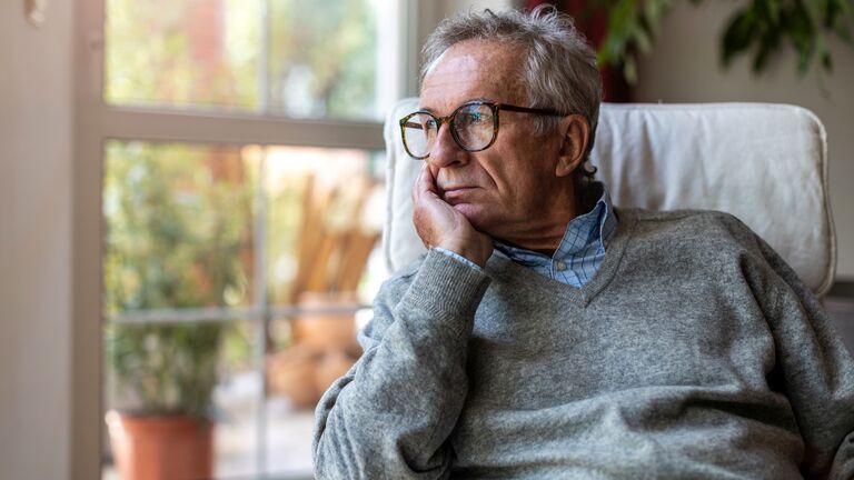 Älterer Mann sitzt am Fenster und schaut nachdenklich hinaus