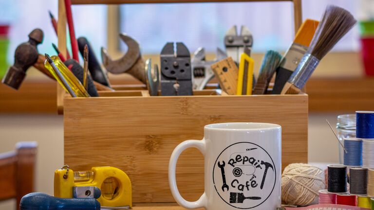 Kaffeetasse mit Repair Cafe-Aufschrift und viel Materialien und Werkzeug für Reparaturen von  Alltagssachen
