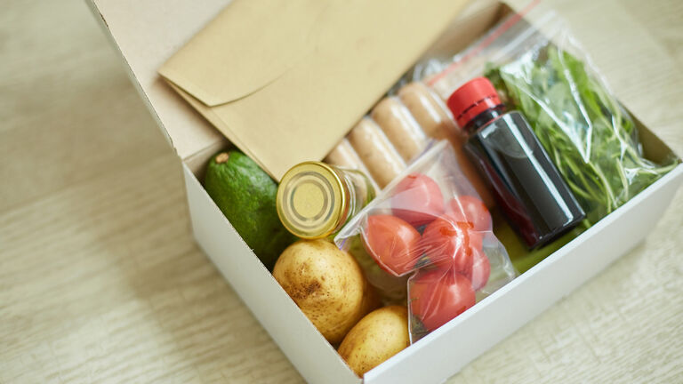 Eine geöffnete Kochbox mit Inhalt aus Zutaten und einem Briefumschlag