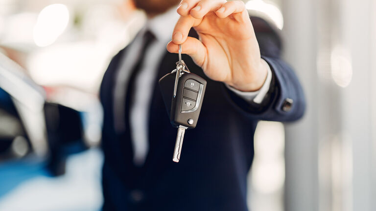 Ein Mann im Anzug (verschwommen dargestellt) hält einen Autoschlüssel in die Kamera
