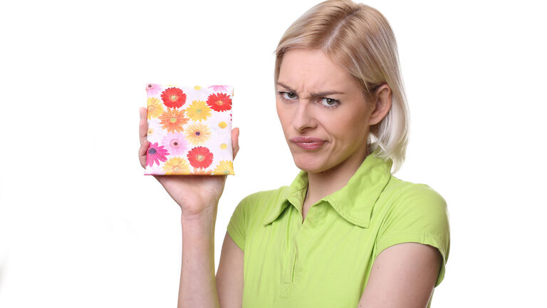 Eine junge Frau hält ein kleines Geschenk in der Hand, macht aber ein unzufriedenes Gesicht