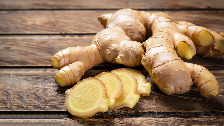 Vor einer Ingwerknolle liegen vier dünne Scheiben Ingwer.