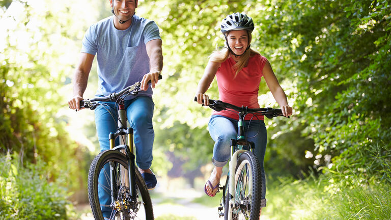 Ein junges Paar mit Fahrradhelmen fährt mit dem Rad einen Waldweg entlang