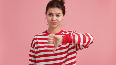 Junge Frau die mit einer Hand den Daumen der linken Hand nach unten streckt und dabei unerfreut schaut