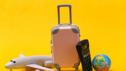 Ein Flugzeug, ein Reisekoffer, ein Taschenrechner und eine kleine Weltkugel bilden ein Stilleben