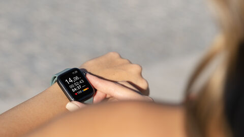 Frau trägt Smartwatch amHandgelenk und schaut auf die erhobenen Daten. Blick ist dabei von oben über die Schulter der Frau.