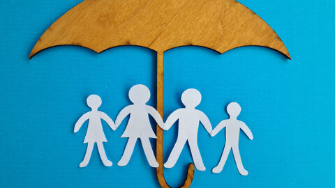 Figuren einer Familie, die aus Papier geschnitten sind werden von einem Schirm aus Holz behütet