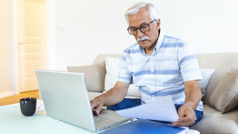 Ein älterer Herr Sitz vor seinem Rechner und hält ein Blatt Papier in der Hand