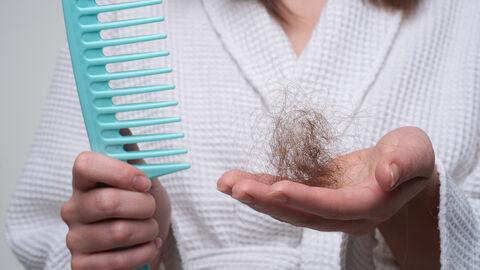 Frau im Bademantel hält Kamm in der rechten Hand und Haarbüschel in der linken Hand