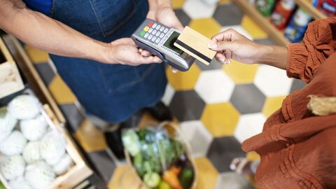 Eine Frauenhand hält eine Bezahlkarte über ein Lesegerät