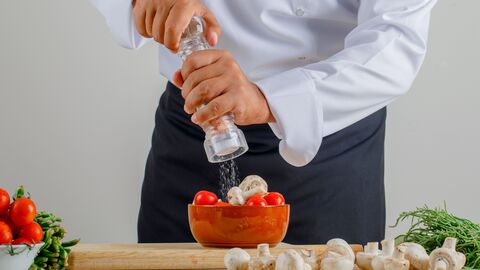 Mann streut Salz mit einer Mühle über den Salat