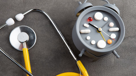 Ein Stethoskop liegt neben einem Wecker, dessen Ziffernblatt setzt sich aus Tabletten zusammen