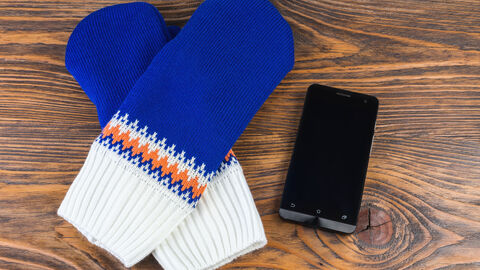 Gestrickte Fäustlinge und Handy auf Holztisch