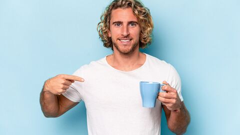 Ein junger Mann deutet auf eine Tasse, die er in der anderen Hand hält