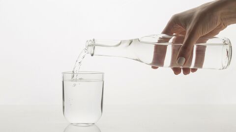 Hand schüttet Wasser in ein Glas