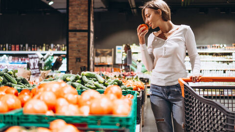 Frau im Supermarkt riecht an einer Tomate