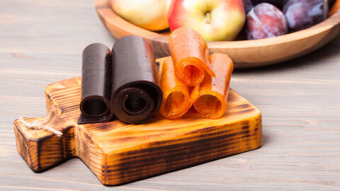 Getrocknetes Fruchtleder, im Hintergrund Zwetschgen und Äpfel in einer Schale