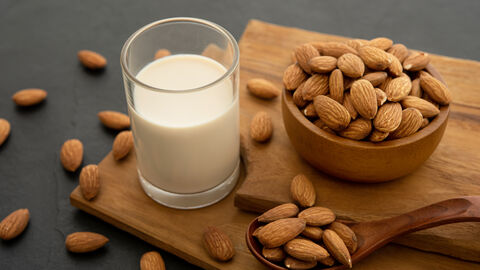Glas Mandelmilch neben Schale und Löffel mit Mandeln