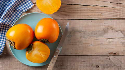 Ganze und aufgeschnittene Kakis auf Teller mit Messer