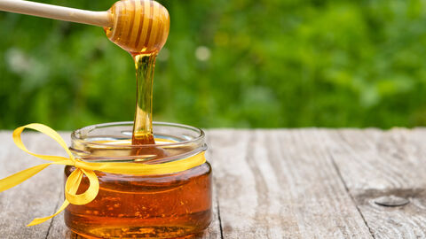 Honig tropft vom Honiglöffel ins Glas