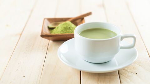 Tasse Matcha-Tee mit Matcha-Pulver im Hintergrund
