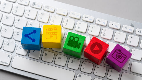 Kleine farbige Holzwürfel mit aufgedruckten Multimedia-Symbolen liegen auf einer Computertastatur