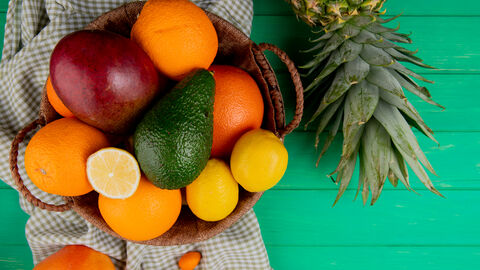 Zitrusfrüchte, Mango und Avocado in Obstkorb neben Ananas