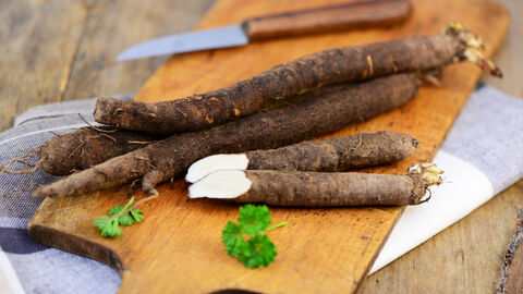 Schwarzwurzeln auf einem Holzschneidebrett, daneben ein Küchenmesser