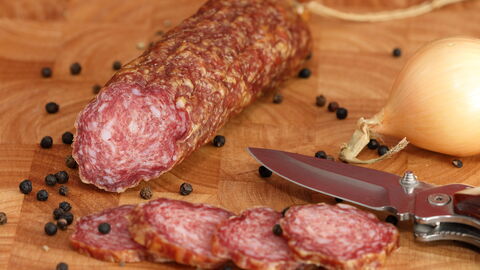 Hessische ahle Wurscht angeschnitten, drum herum Pfefferkörner und eine Zwiebel