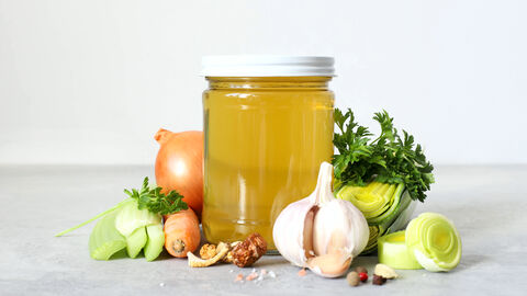 Selbstgemachte Gemüsebrühe im Schraubglas, drum herum Suppengemüse, Zwiebeln und Knoblauch