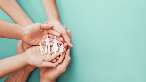 Kinder und Erwachsenenhände halten aus Holz ausgeschnittene Figuren, die eine Familie darstellen